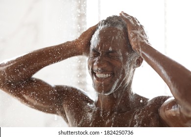 Black Man Washing Head And Body Using Male Shampoo Taking Shower Standing Under Water Drops In Bathroom At Home. Haircare Cosmetics For Men, Male Hygiene Routine Concept