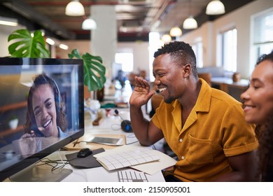 A Black man waves to his colleague on a video call from his office