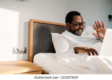 Black Man Waving Hand And Using Laptop While Resting In Bed At Home