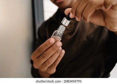 Black Man Wearing Bathrobe Applying Face Serum At Morning In Bathroom