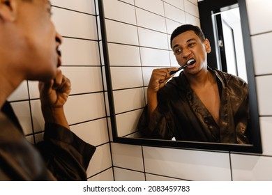 Black Man Wearing Bathrobe Brushing His Teeth At Morning In Bathroom