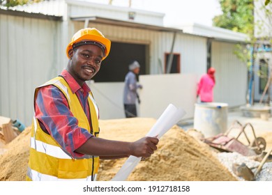 A Black Man Wearing A Safety Suit And A Hard Hat Holding A Paper In Hand, And He Looking At The Camera Within A Construction Site.