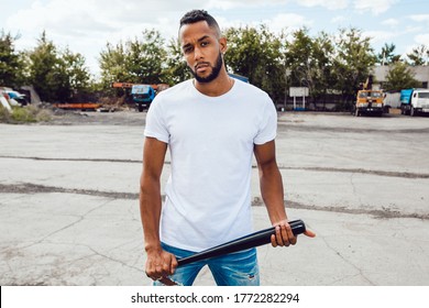 Black Man In A White T-shirt With A Bat In His Hands Stands On The Street.