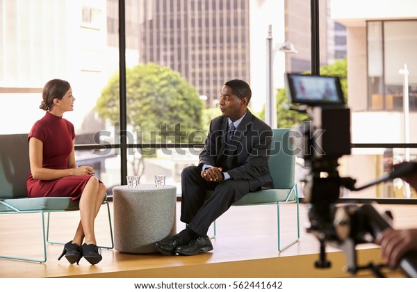 Black\
man and white woman on set filming a TV\
interview