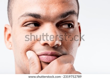 A black man's close-up portrait. He's either pondering a lucrative idea or doubting someone's integrity, as he pensively rubs his lower face