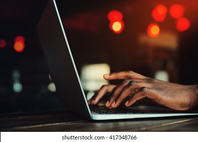 Black man's hands typing on laptop keyboard. Person working with laptop. Beautiful lights as background. Toned style instagram filters. Selective focus 
