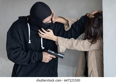 Black masked robber in black long sleeve shirt is holding a gun and intimidate a woman , he is pulling her hair. Woman is try to fight and disobey.