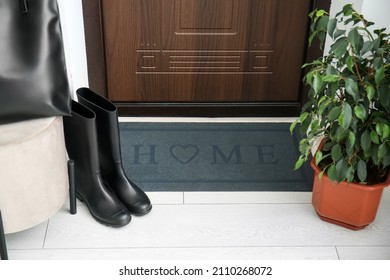 Black Mat With Gumboots And Houseplant Near Dark Wooden Door