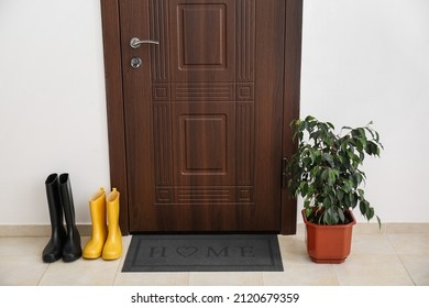 Black Mat With Gumboots And Houseplant Near Dark Wooden Door