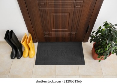 Black Mat With Gumboots And Houseplant Near Dark Wooden Door