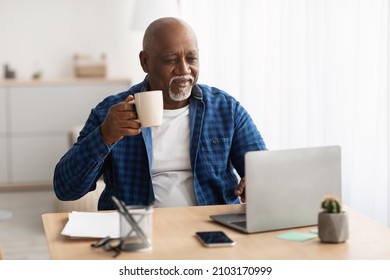 Black Mature Man Working Online On Laptop Computer And Drinking Coffee Sitting At Workplace In Modern Office. Entrepreneurship Career And Freelance Job In Senior Age Concept