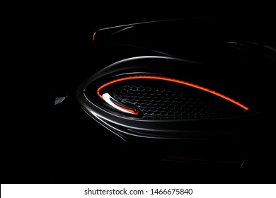 Black Mclaren 570s rear left tail light illuminated, shot against a dark background featuring a rear wing mounted to the car.