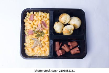 A Black Meal Box Consist Of Mac And Cheese, Cheese Bread Balls And Beef Sausages On White Background, High Angle View