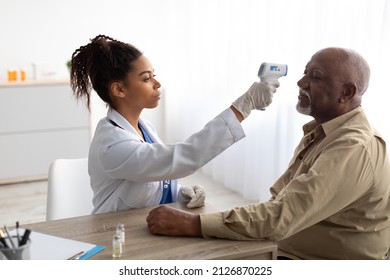 Black Medical Worker Doing Temperature Screening For Elderly Patient Man Measuring Fever Before Vaccination Using Contactless Infrared Themometer. Coronavirus Protection In Hospital Concept