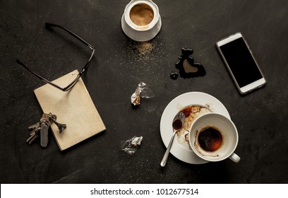 Black Messy Cafe Table - Empty Coffee Cup, Book, Mobile Phone (smartphone), Glasses And Keys. Dark Moody Layout Captured From Above (flat Lay, Top View).