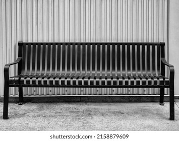 Black Metal Bench Against A Corrugated Metal Wall.