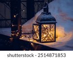 Black metal candle lantern with led lights sting inside in the winter outdoors. Snowy wood patio in the night, during Christmas holidays.