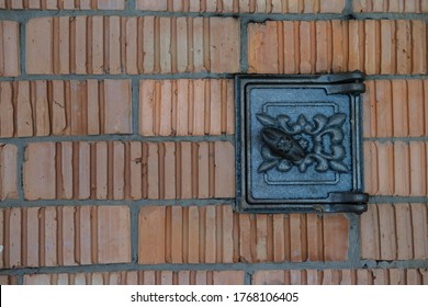 Black Metal Door For Cleaning A Wood Stove Or Fireplace From Soot And Dirt, On A Background Of Red Brick.