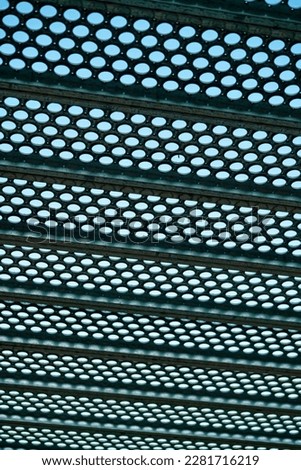 Black metal grate or drain vent with holes in geometric pattern for background or texture image with background sky. In industrial area with light pattern and horizonal beams in city.