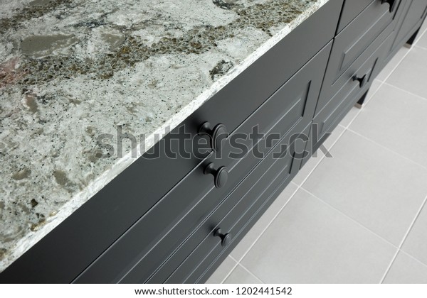 Black metal handles on wooden\
drawer and front door of kitchen cabinet under stone worktop\
.