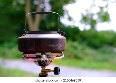 Black Metal Tourist Kettle Is Heated On Open Flame On Gas Burner In Forest, Concept Of Hiking In Nature, Tourism, Orienteering, Couple Camping, Adventure As They Pitch A Camp In Nature’s Great Expanse