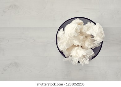 Black Metal Trash Bin Full Of Crumpled Waste Paper On White Wooden Floorboard. Top Down View.