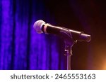 black Mic microphone mike with round head chrome on a stand ready for performer set against velvet blue curtain and a stagelight spotlight in bottom corner in theatre on stage