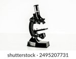 A black microscope is sitting on a white surface. The microscope is black and white, and it is the only object in the image