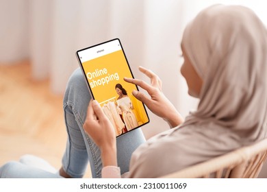 Black millennial arab woman in hijab using tablet with fashion store on screen, choose clothes at home. Shopaholic customer pay for order, delivery with app and website, enjoy online shopping - Powered by Shutterstock