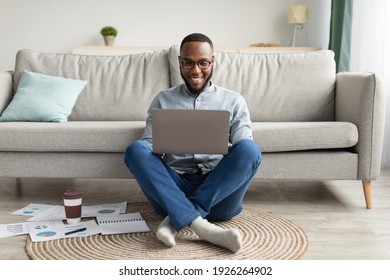 Black Millennial Man Using Laptop Computer Browsing Internet Working Online Sitting On Floor At Home. Successful Freelancer. Distant Job And Freelance Career Concept