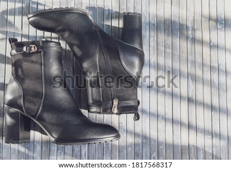 Black mixed leather cowboy boots lie on the left against a gray wood background with space for text on the right, close-up top view.