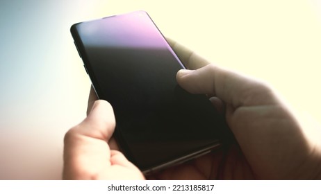 Black Mobile Phone Turned Off On A White Table With A Man's Hands Next To It Waiting For A Call