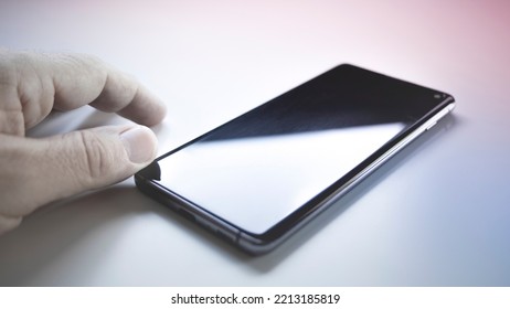 Black Mobile Phone Turned Off On A White Table With A Man's Hands Next To It Waiting For A Call