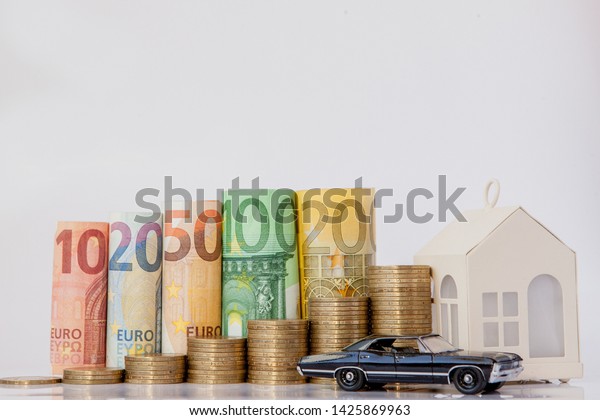 A black model of a car, house and ten, twenty,\
fifty, one hundred, two hundred and coins euro rolled bills\
banknotes on white background. Histogram from the euro. Concept of\
currency growth, savings