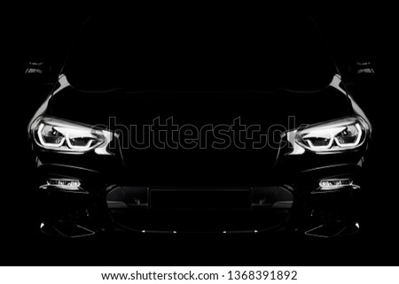 Black modern car headlights - front view. Silhouette of black sports car with headlights on black background.