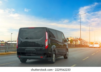Black modern passenger charter van with a small delivery moves fast on the highway to the urban suburbs. Business distribution and logistics express service. Mini bus rides along the highway