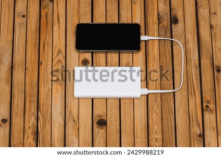 A black modern smartphone, a phone with a battery with a large display, is charged with energy through a cable from a white power bank without electricity. Photography, usb technology concept.