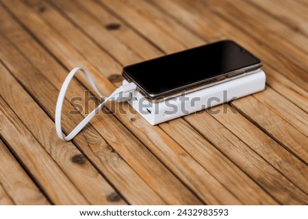 A black modern smartphone, a phone with a battery with a large display, is charged with energy through a cable from a white power bank without electricity. Photography, USB technology.