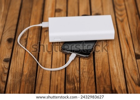 A black modern smartphone, a phone with a battery with a large display, is charged with energy through a cable from a white power bank without electricity. Photography, usb technology concept.