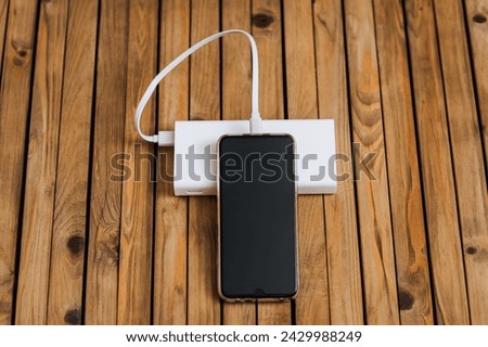 Black modern smartphone, a phone with a dead battery is charged with energy through a long cable from a white power bank without electricity. Close-up photography, usb technology concept.
