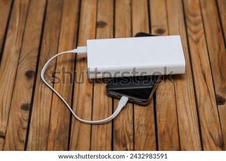 Black modern smartphone, a phone with a dead battery is charged with energy through a cable from a white power bank without electricity. Photography, usb technology concept.