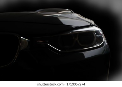 Black modern sport luxury car led xenon headlights - front view with black background in the garage