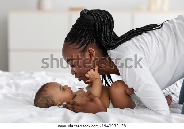 Black\
mom playing in bed with her infant, kissing\
baby