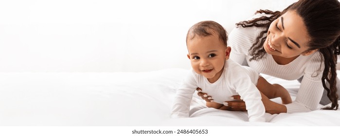 Black Mom Posing With Baby Toddler Holding Helping Her Son Crawl On White Studio Background. Happy Young Mother Caring For Child Infant Bonding And Playing With Cute Little Boy. Panorama, Copy Space - Powered by Shutterstock