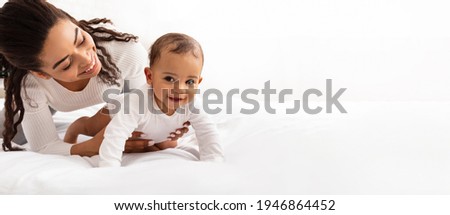 Black Mom Posing With Baby Toddler Holding Helping Her Son Crawl On White Studio Background. Happy Young Mother Caring For Child Infant Bonding And Playing With Cute Little Boy. Panorama, Copy Space