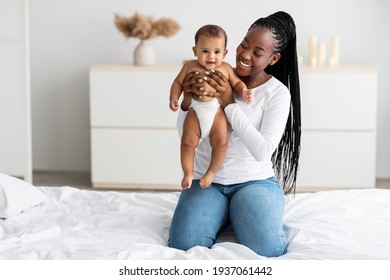 Black mom sitting on bed with her cute little baby