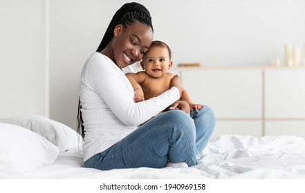 Black mom sitting on bed with her cute baby