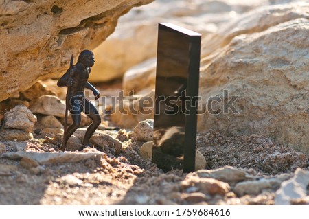 Black monolith on old sandstone rock near the sea coast and Cro-Magnon man with spear