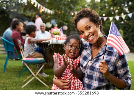 Black mother and baby hold flag at 4th July party, to camera