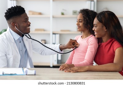 Black mother and daughter having checkup at pediatrician, cheerful african american girl sitting on mom lap and smiling while male dctor checking up her chest with stethoscope, clinic interior - Powered by Shutterstock